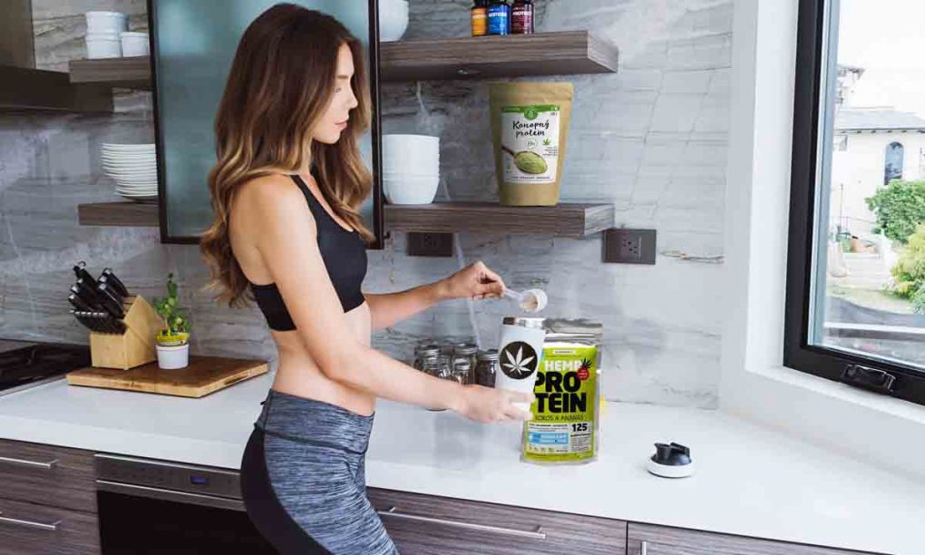 Mladá žena si v kuchyni pripravuje nápoj s konopným proteínom